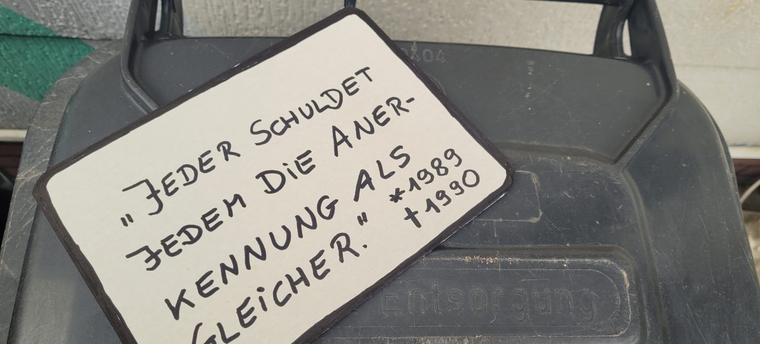 Schild mit Zitat "Jeder schuldet jedem die Anerkennung als Gleicher." auf Mülltonne